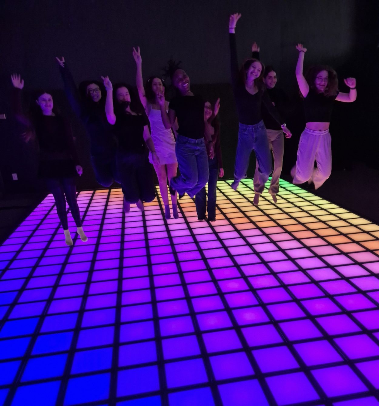 A group of friends jumping together on the jeuLumi LED floor lit in purple and blue